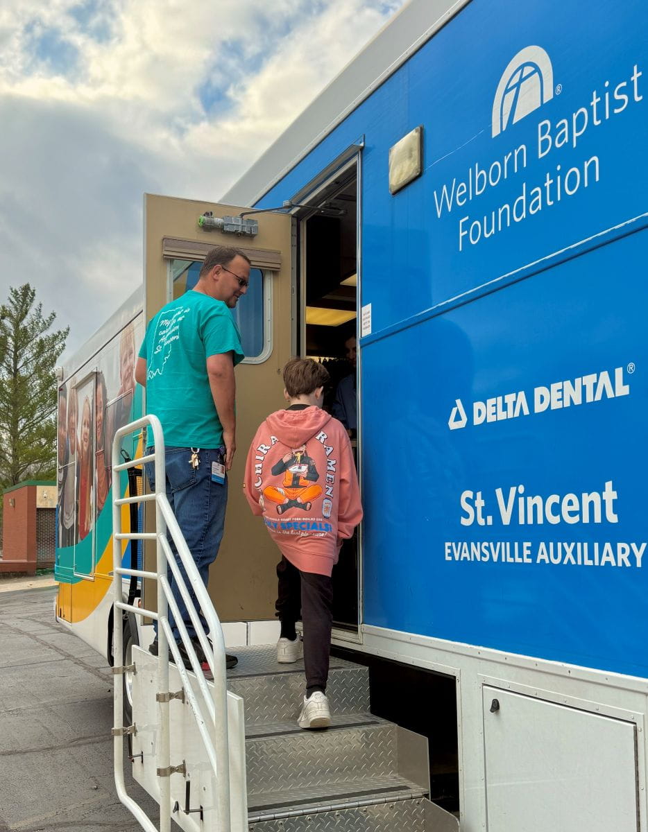 A child with a colorful backpack enters a mobile dental clinic with man opening the door.